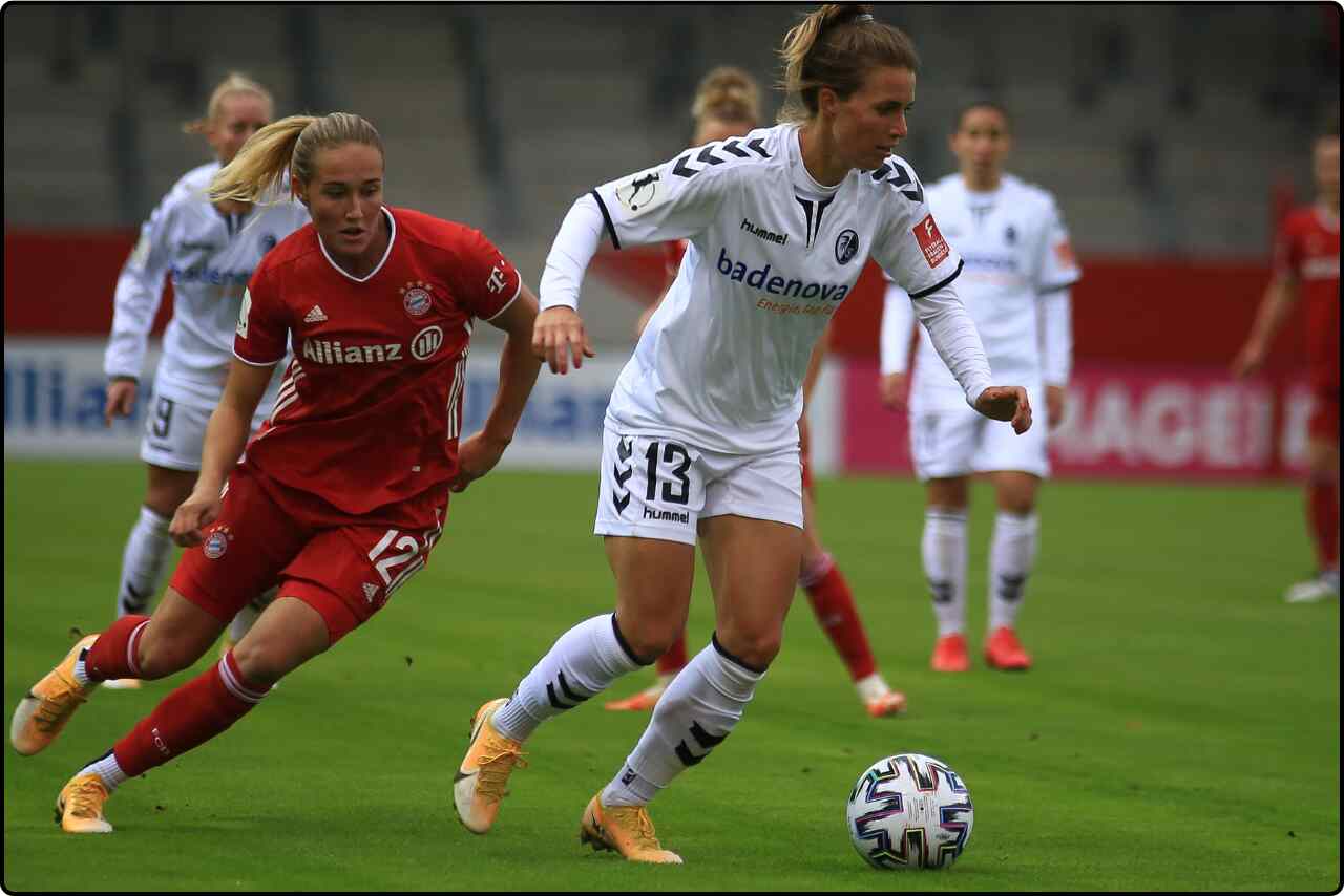 Two women soccer players in action, one attempting to tackle the ball while the other is in mid-stride.